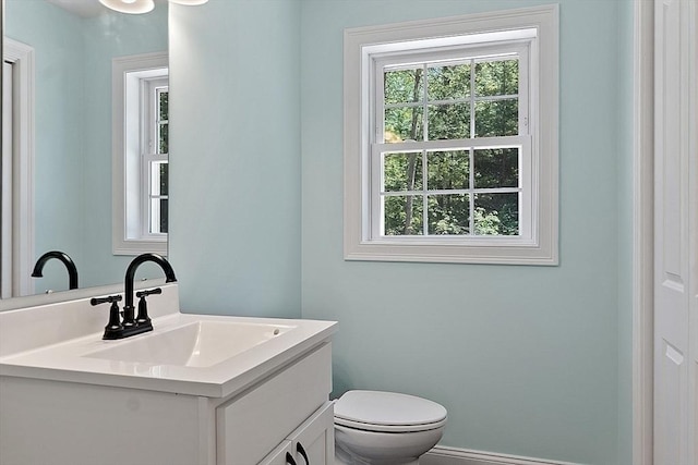 half bath with toilet, baseboards, and vanity