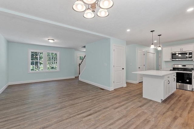 kitchen featuring a center island, wood finished floors, stainless steel appliances, white cabinetry, and baseboards