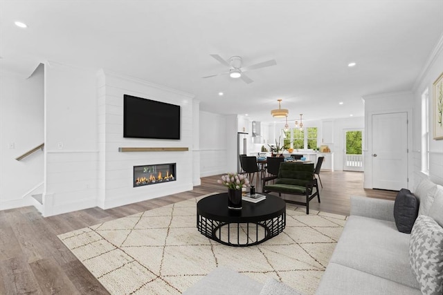 living room featuring ceiling fan, a large fireplace, light wood-type flooring, and ornamental molding