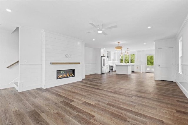 unfurnished living room with hardwood / wood-style floors, a large fireplace, ceiling fan, and crown molding