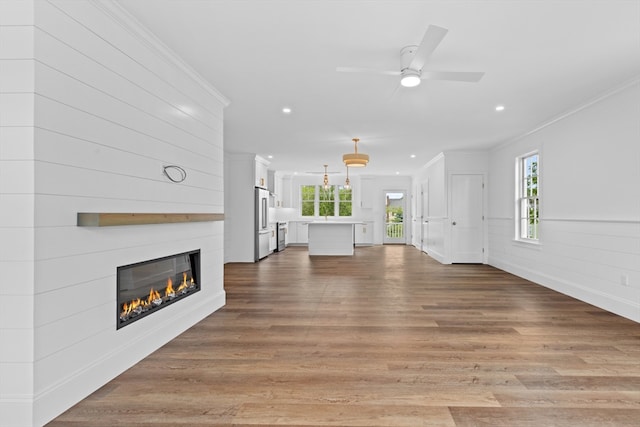 unfurnished living room with ceiling fan, a fireplace, hardwood / wood-style flooring, and ornamental molding