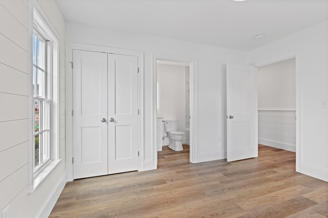 unfurnished bedroom featuring ensuite bath, a closet, light hardwood / wood-style floors, and multiple windows