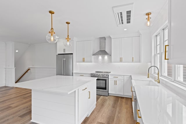 kitchen with light stone countertops, a center island, wall chimney range hood, white cabinets, and appliances with stainless steel finishes