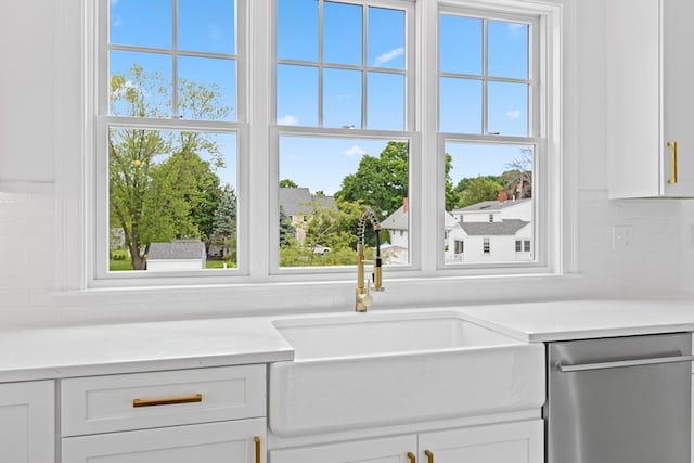 interior space featuring light stone counters, a wealth of natural light, sink, dishwasher, and white cabinetry