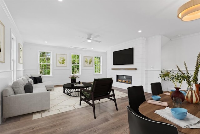 living room with crown molding, a large fireplace, ceiling fan, and light hardwood / wood-style floors