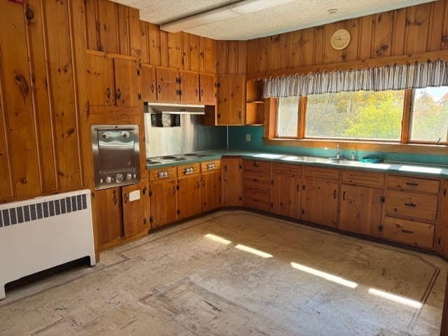 kitchen with wooden walls, radiator heating unit, sink, and a textured ceiling