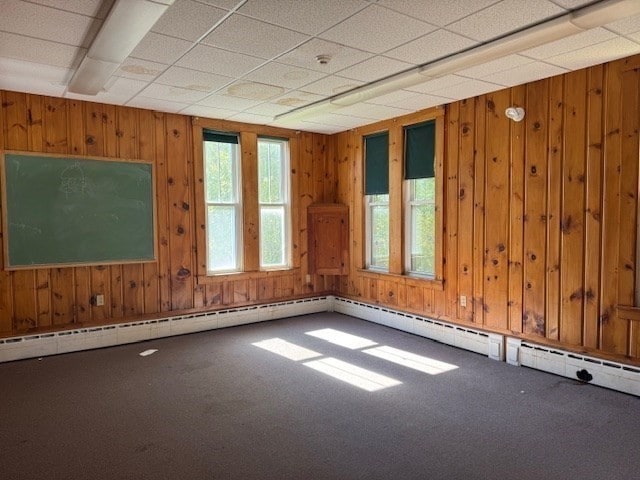 carpeted empty room featuring a drop ceiling and wood walls