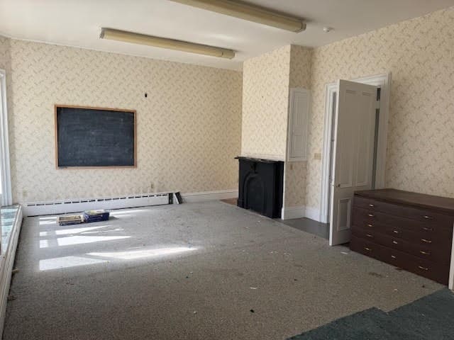 unfurnished living room featuring carpet floors and baseboard heating