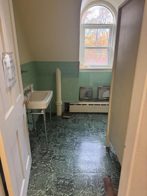 bathroom featuring baseboard heating, sink, and tile walls