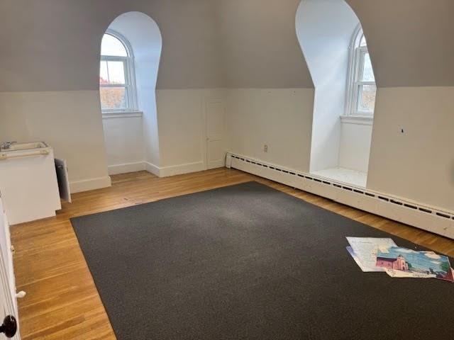 additional living space featuring lofted ceiling, baseboard heating, and hardwood / wood-style floors