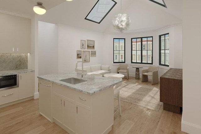kitchen featuring a sink, light wood finished floors, white cabinetry, and lofted ceiling