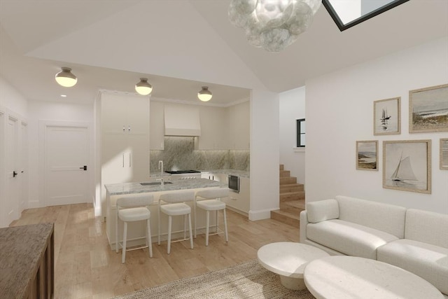 living area with light wood-style flooring, stairs, a skylight, and high vaulted ceiling