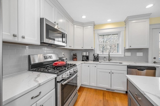 kitchen with a sink, appliances with stainless steel finishes, light wood-style flooring, and white cabinets