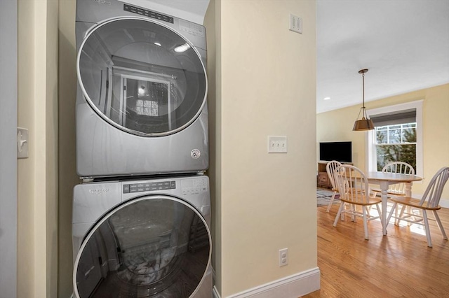 laundry area with baseboards, wood finished floors, and stacked washing maching and dryer