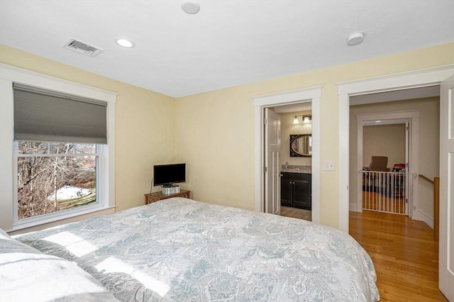 bedroom with visible vents, recessed lighting, ensuite bath, and wood finished floors