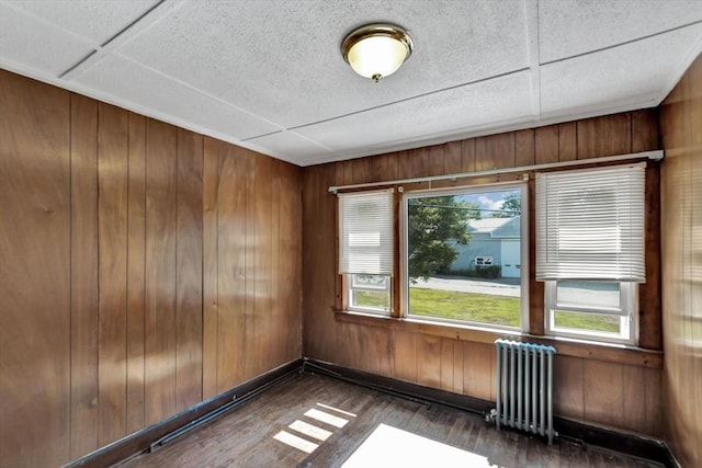 unfurnished room with radiator, hardwood / wood-style flooring, baseboards, and wood walls