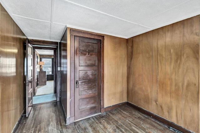 empty room featuring dark wood finished floors, wood walls, and baseboards