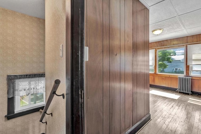 details featuring a paneled ceiling, wooden walls, radiator heating unit, and wood finished floors