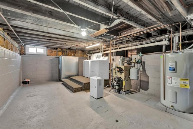 below grade area featuring concrete block wall, washer and clothes dryer, water heater, freestanding refrigerator, and a heating unit