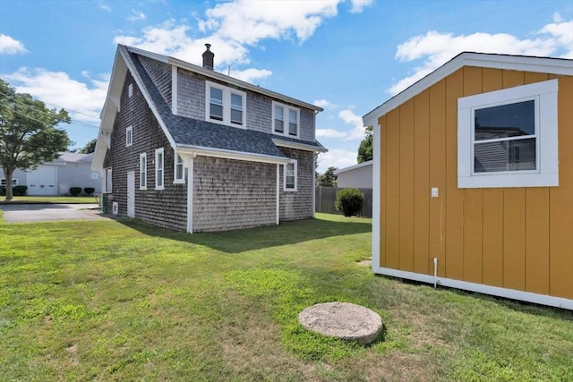 back of house featuring a shingled roof, a chimney, a lawn, and an outdoor structure