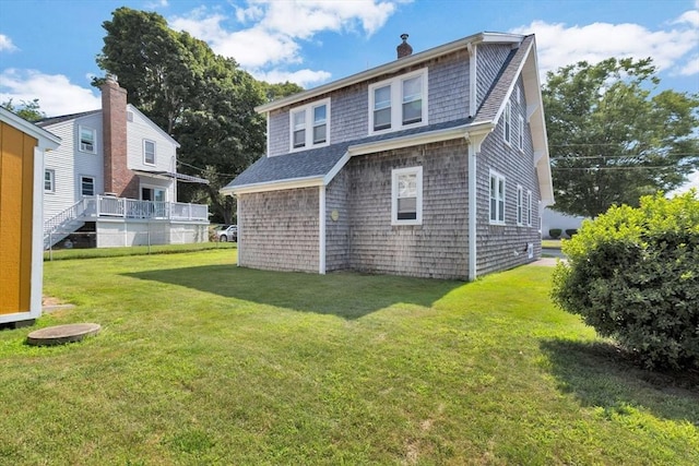 rear view of house featuring a chimney, a lawn, and roof with shingles