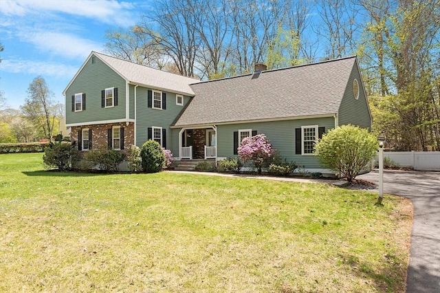 view of front facade featuring fence, a front yard, roof with shingles, a chimney, and brick siding