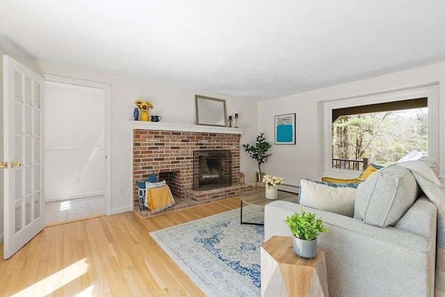living area featuring french doors, a brick fireplace, a baseboard heating unit, and wood finished floors
