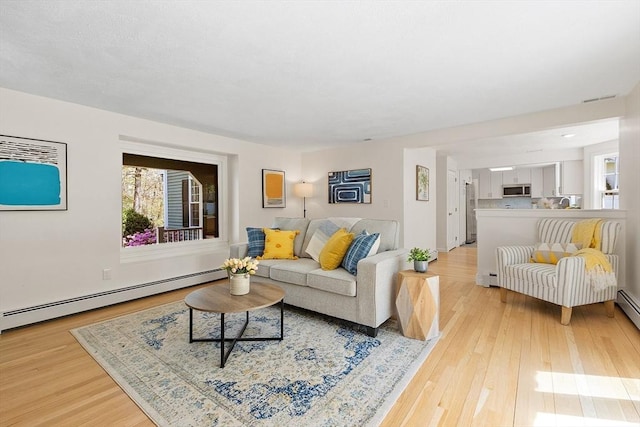 living area with light wood-style floors, a baseboard heating unit, and a healthy amount of sunlight