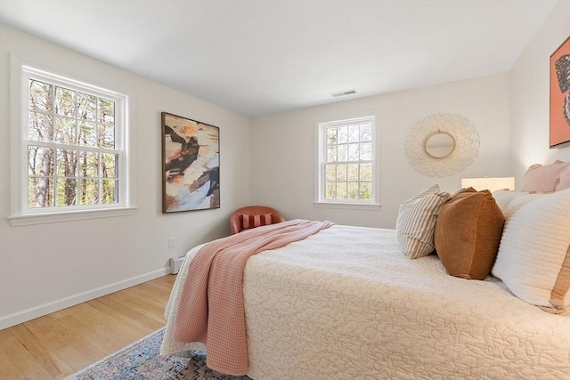 bedroom with baseboard heating, baseboards, visible vents, and wood finished floors