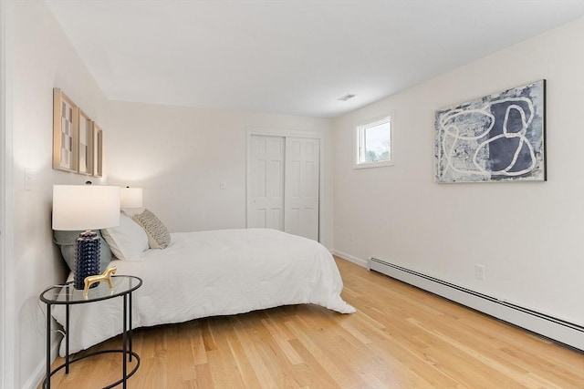 bedroom featuring visible vents, a closet, light wood-style floors, baseboards, and a baseboard radiator