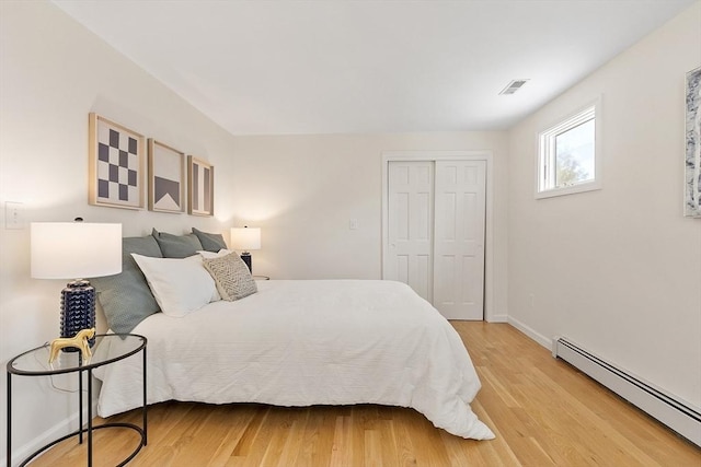 bedroom featuring visible vents, baseboard heating, light wood-type flooring, baseboards, and a closet
