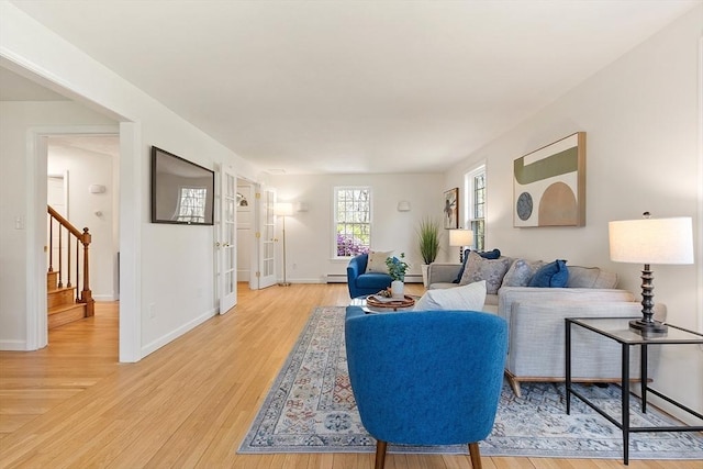 living area with stairway, baseboards, a baseboard heating unit, and light wood-style flooring