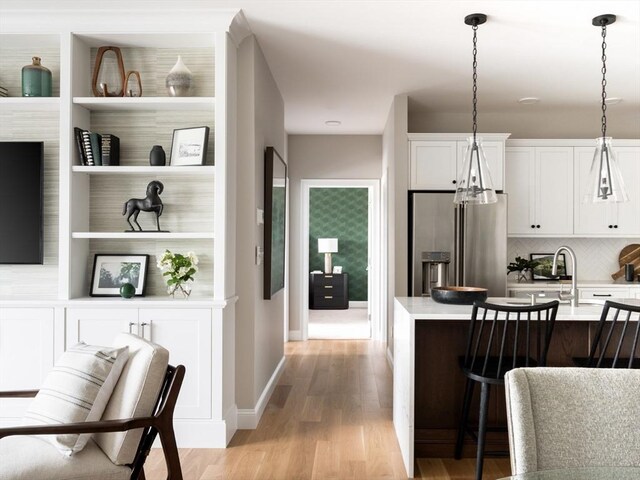 kitchen with high quality fridge, light wood-type flooring, decorative backsplash, light countertops, and a breakfast bar area