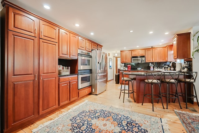 kitchen featuring appliances with stainless steel finishes, a kitchen bar, light wood-type flooring, and tasteful backsplash