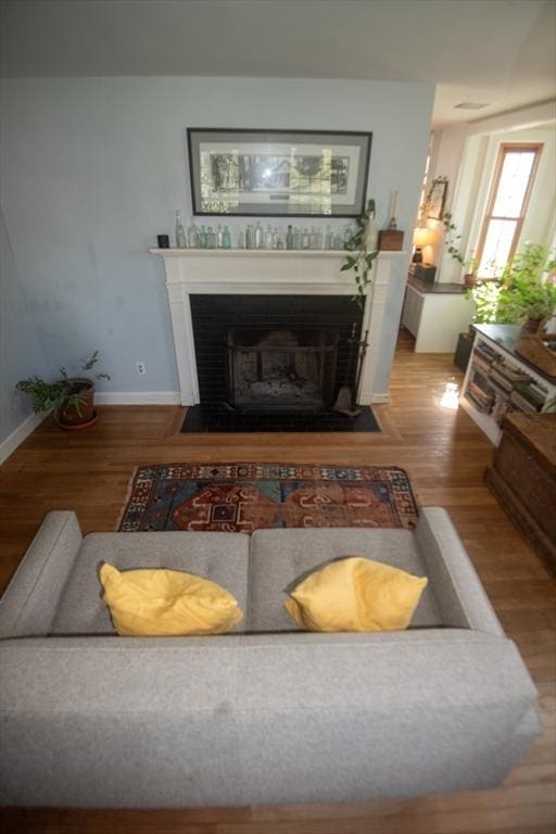 living room featuring a fireplace with flush hearth, wood finished floors, and baseboards