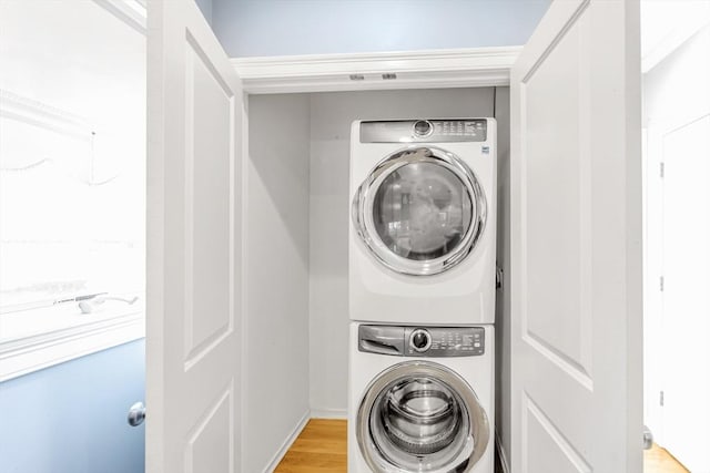 clothes washing area featuring laundry area, light wood finished floors, and stacked washer / dryer