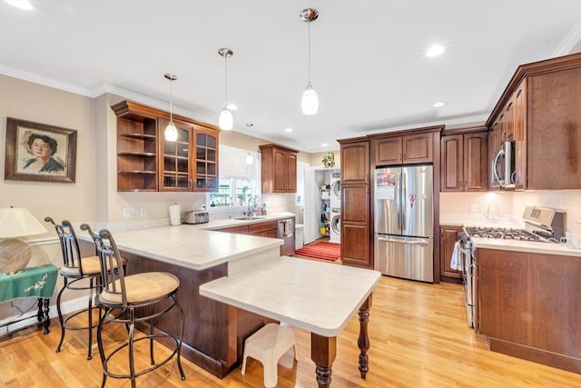 kitchen featuring a kitchen bar, a sink, light wood finished floors, a peninsula, and stainless steel appliances