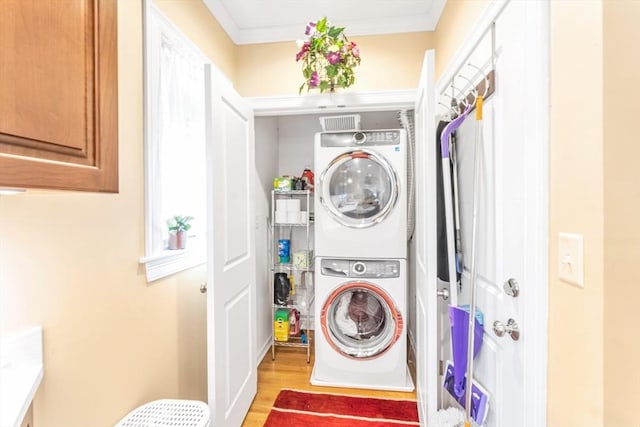 laundry room with crown molding, stacked washer and clothes dryer, wood finished floors, and laundry area