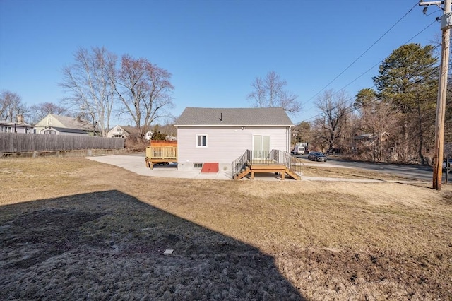 back of property with a deck, fence, and a lawn