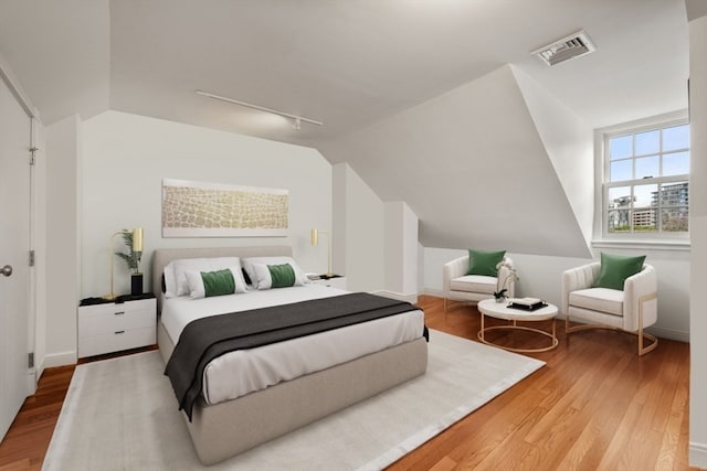 bedroom featuring vaulted ceiling, light wood-type flooring, and track lighting