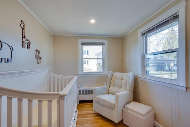 bedroom featuring ornamental molding, a nursery area, radiator, and light wood-type flooring