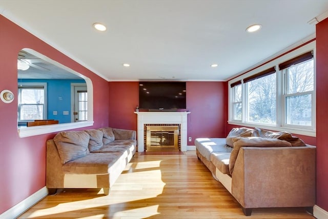 living room with ceiling fan, a brick fireplace, crown molding, and light wood-type flooring