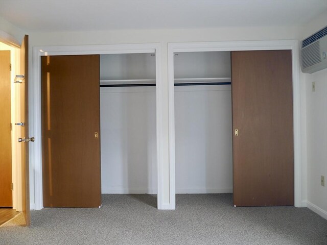 unfurnished bedroom with an AC wall unit, light colored carpet, and multiple closets