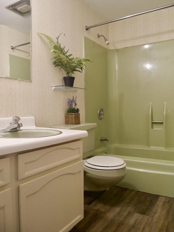 bathroom featuring wallpapered walls, shower / tub combination, wood finished floors, and vanity