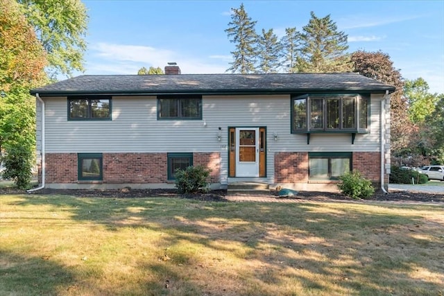 raised ranch featuring brick siding, a chimney, and a front yard