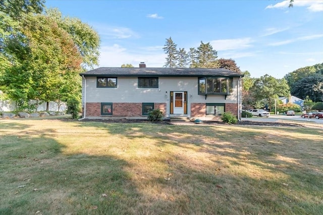 split foyer home featuring brick siding, a chimney, and a front yard