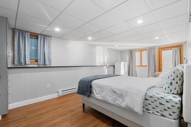 bedroom with a baseboard radiator, recessed lighting, a paneled ceiling, wood finished floors, and baseboards