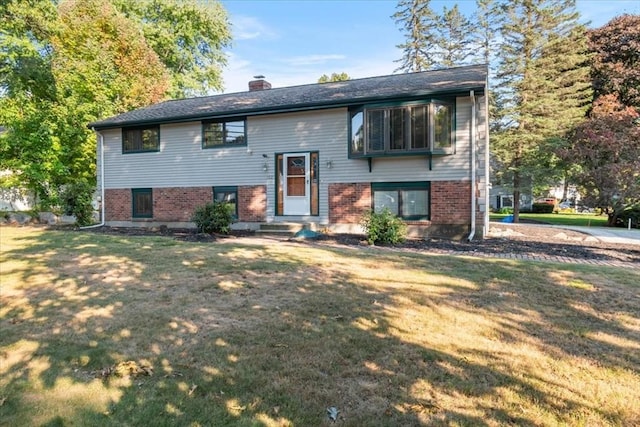 split foyer home featuring a front lawn, a chimney, and brick siding