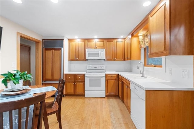 kitchen with white appliances, brown cabinets, light countertops, light wood-style floors, and a sink