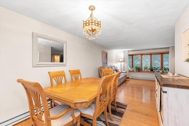 dining space featuring a chandelier, light wood finished floors, and baseboard heating